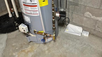 A water heater with connected pipes and valves in a basement setting.