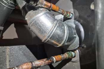 Pipes and a metal duct connected to a black housing unit with visible wear and corrosion.