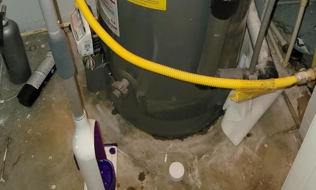 A water heater surrounded by cleaning tools and pipes on a concrete floor.
