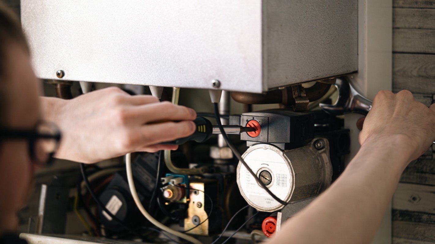A person is using a screwdriver to work on a mechanical device with various visible components.