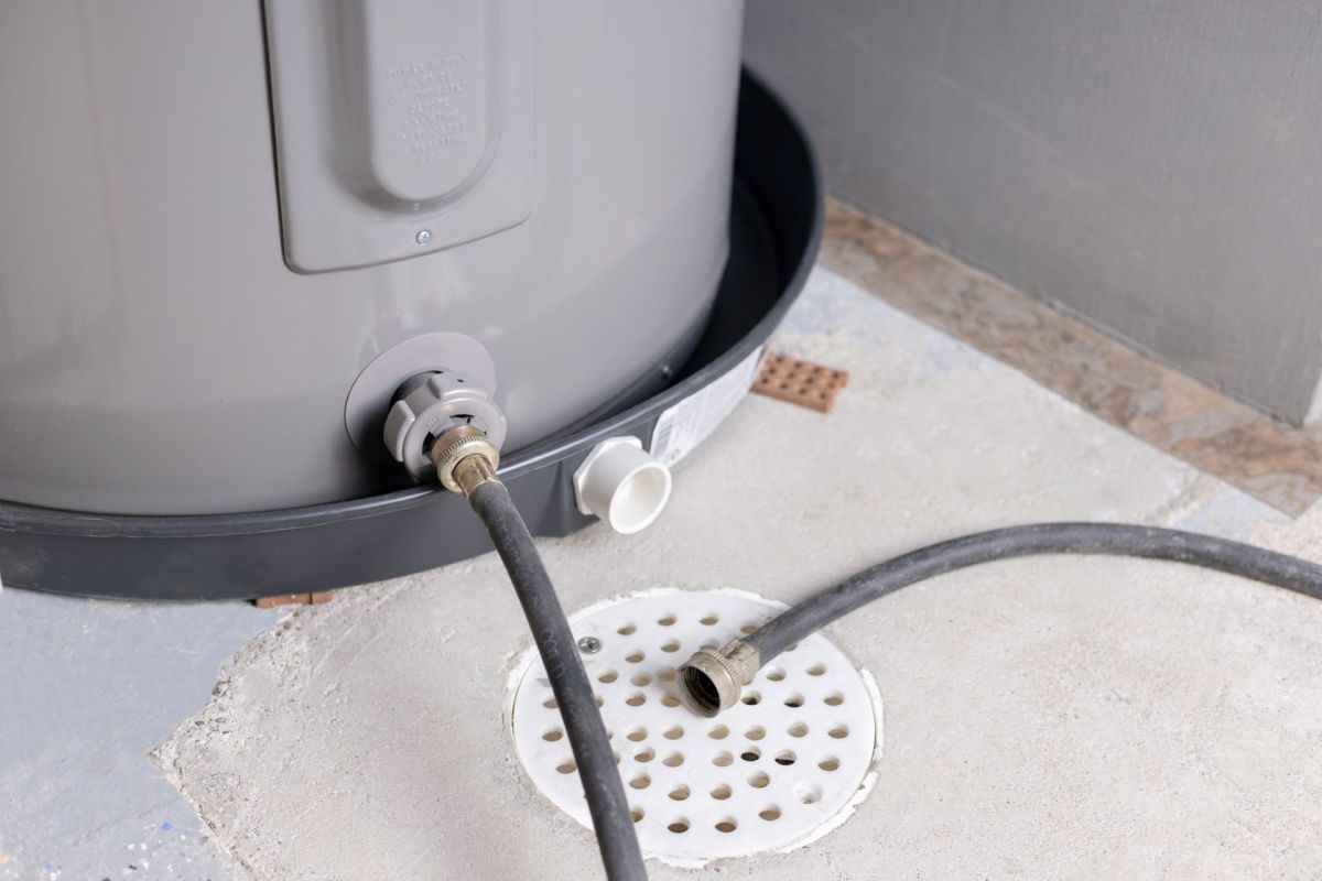 A gray water heater connected to a drainage hose on a concrete floor.