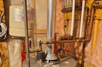 A water heater with connected pipes and a gas tank in an insulated basement.