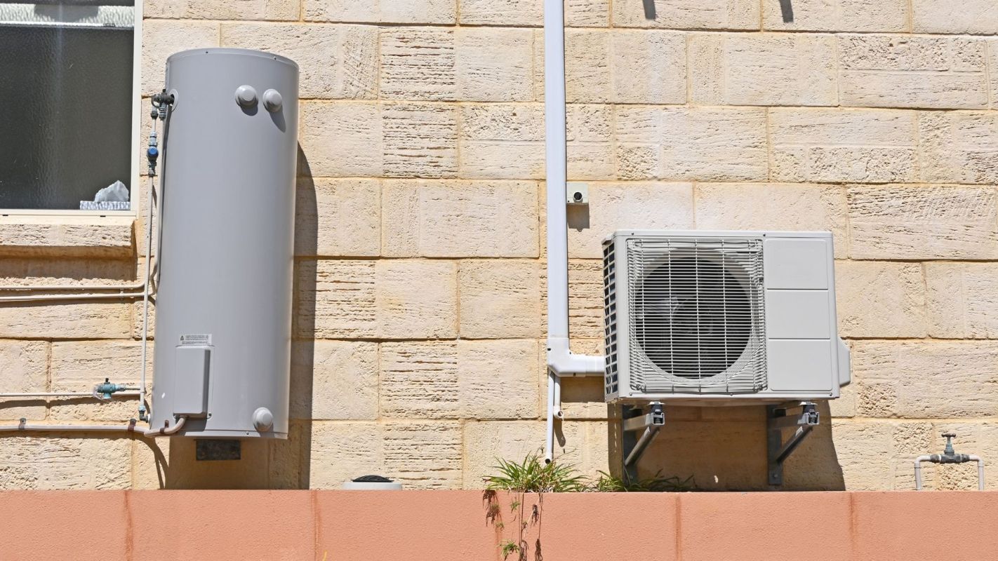 A hot water tank and a heat pump attached to the exterior of a building
