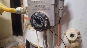 A water heater control valve with warning labels and exposed wiring connections.