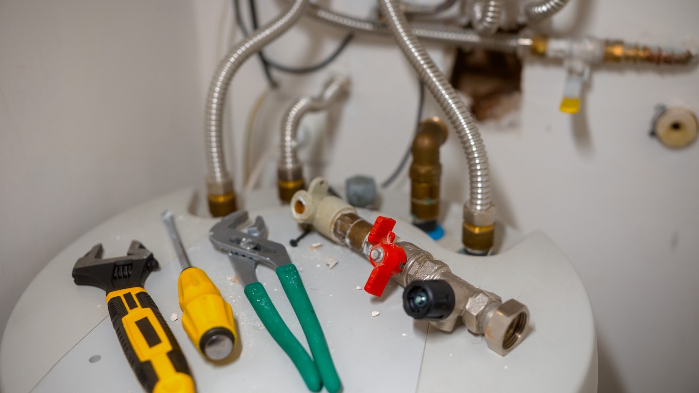 Tools and plumbing connections are arranged on top of a water heater.