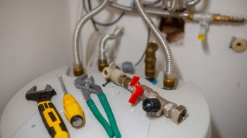 Tools and plumbing connections are arranged on top of a water heater.