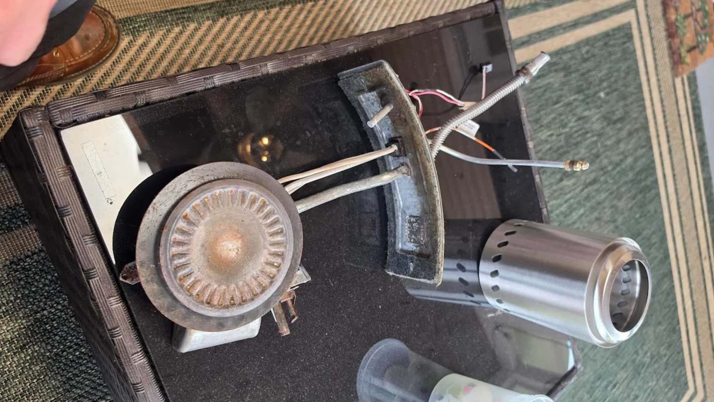 A disassembled gas burner with metal components on a dark surface.