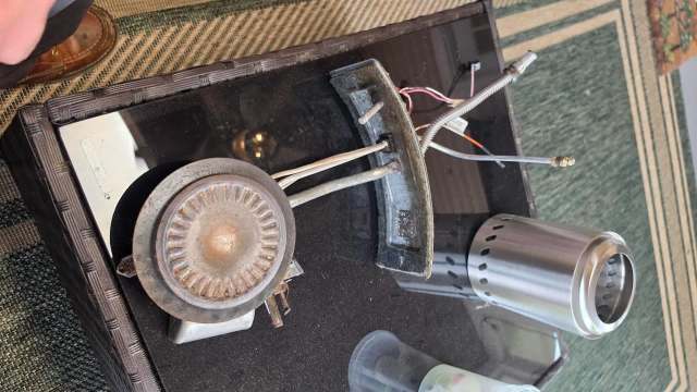 A disassembled gas burner with metal components on a dark surface.