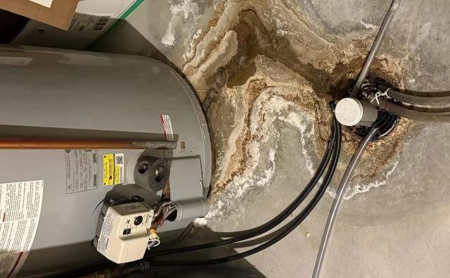 Water heater with a stained floor and drainage pipe, showing signs of water damage and mineral deposits.
