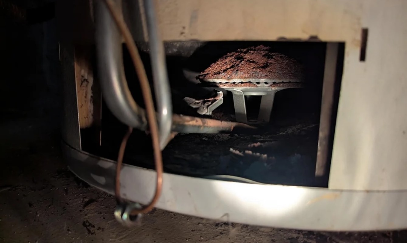 Rust buildup visible from the bottom of a metal water boiler, surrounded by dirt and debris.