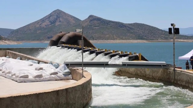 Water flows from a pipe into a reservoir of a treatment plant with mountains in the background.