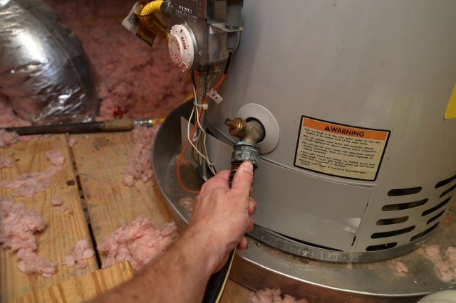 A person attaching a hose to a water heater.