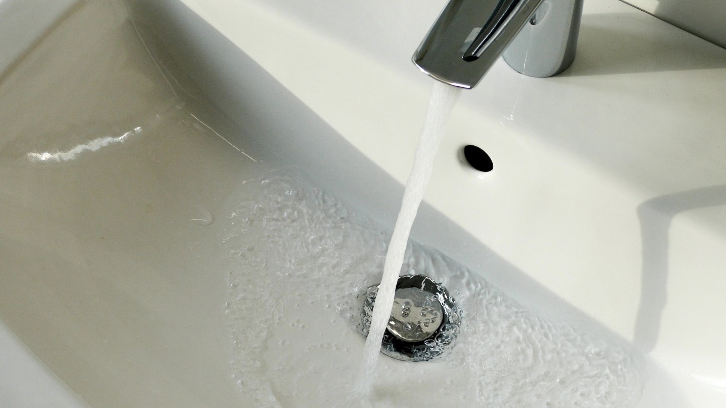 Water flows from a faucet into a white sink, creating bubbles.