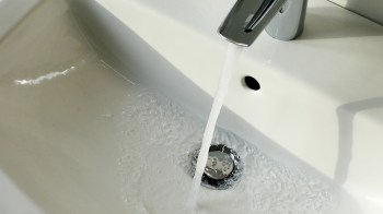 Water flows from a faucet into a white sink, creating bubbles.