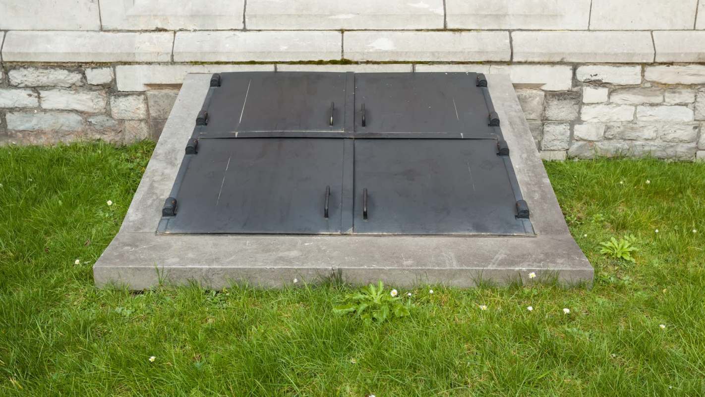 A square set of black metal access doors on a stone base in a grassy area.