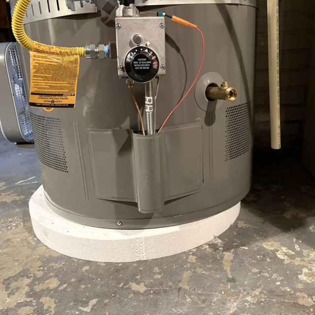 A water heater sitting partly off its base.