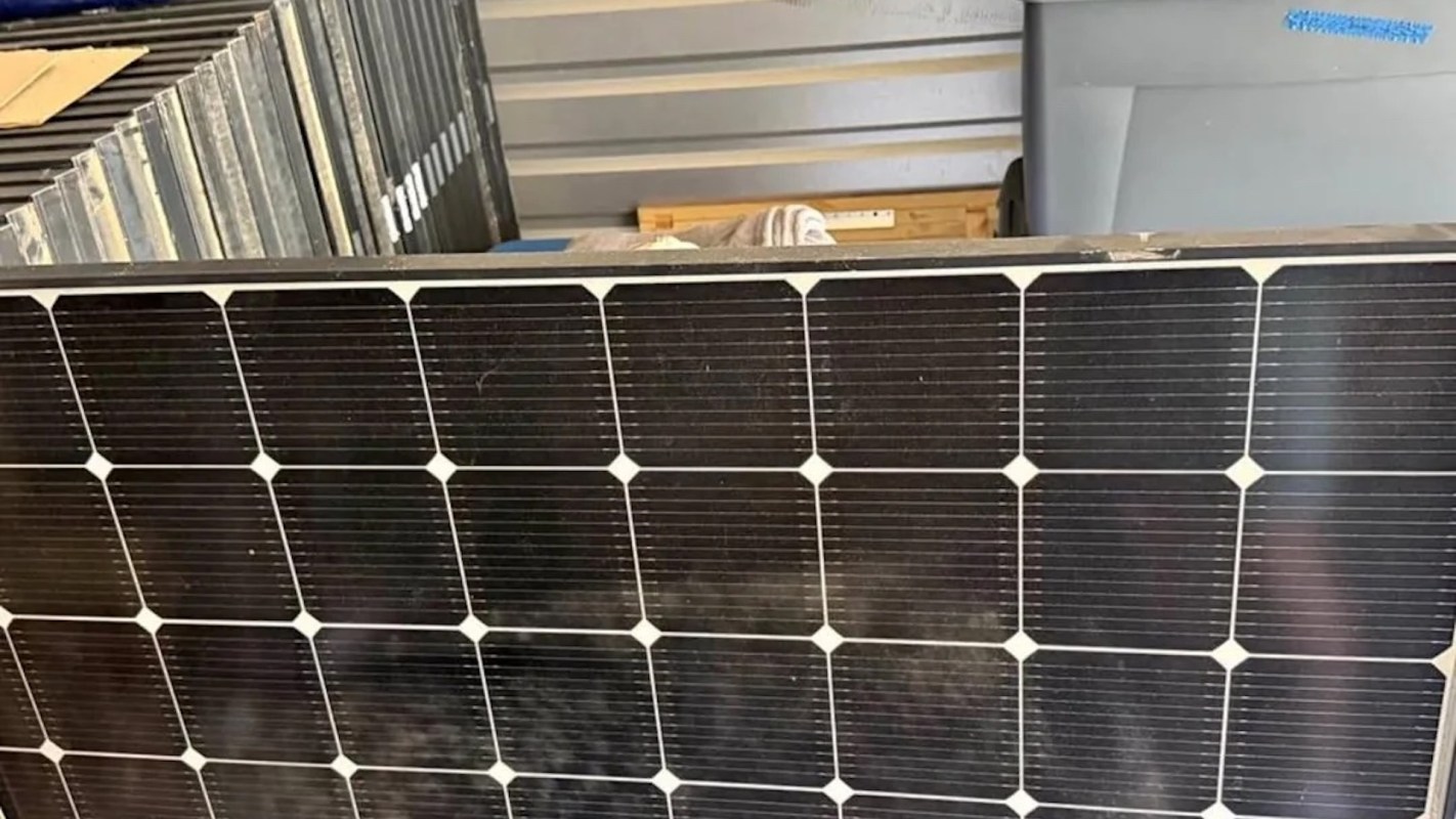 A solar panel with a grid pattern of dark cells and white connectors, set against a storage environment.