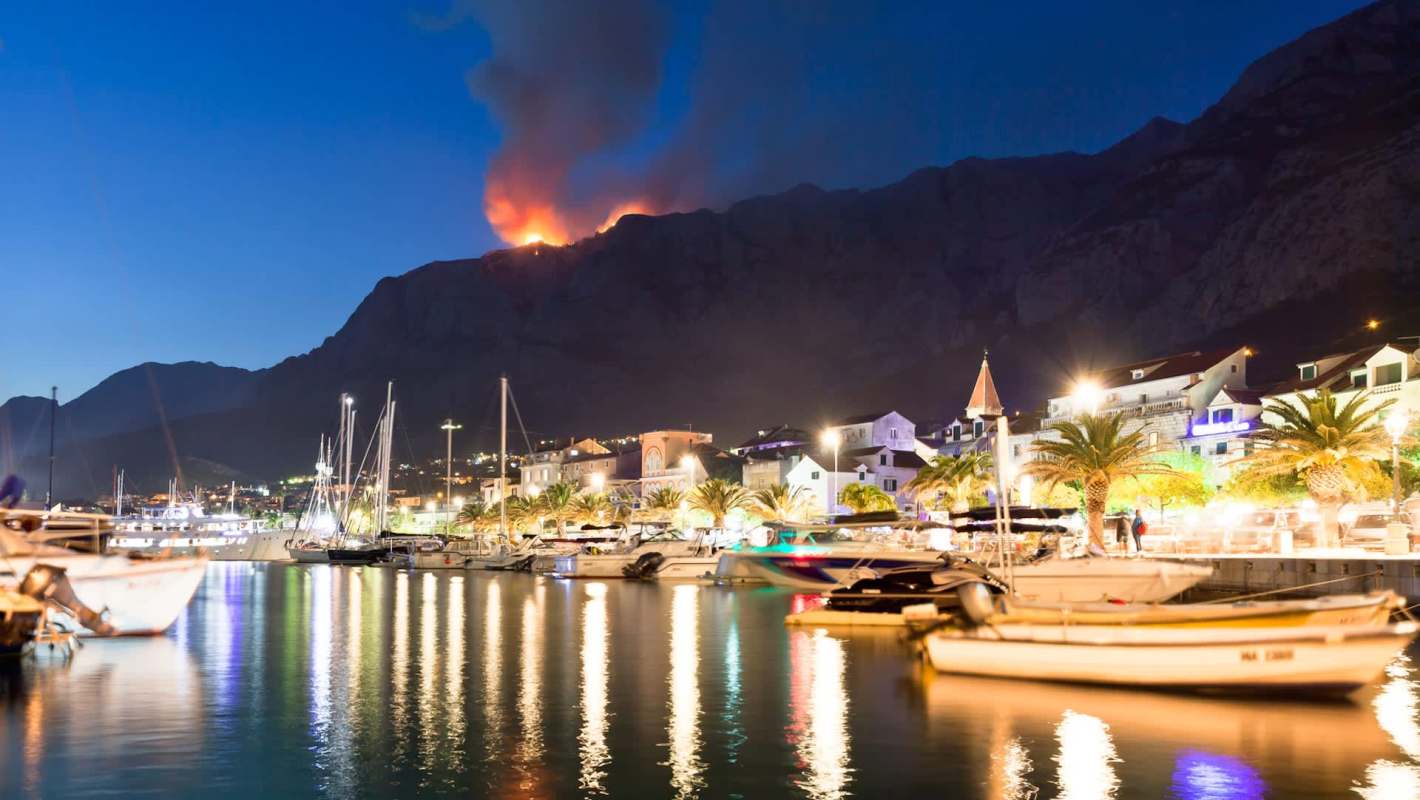 A wildfire on a mountain near boats.