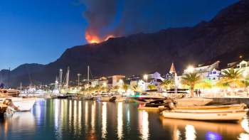 A wildfire on a mountain near boats.