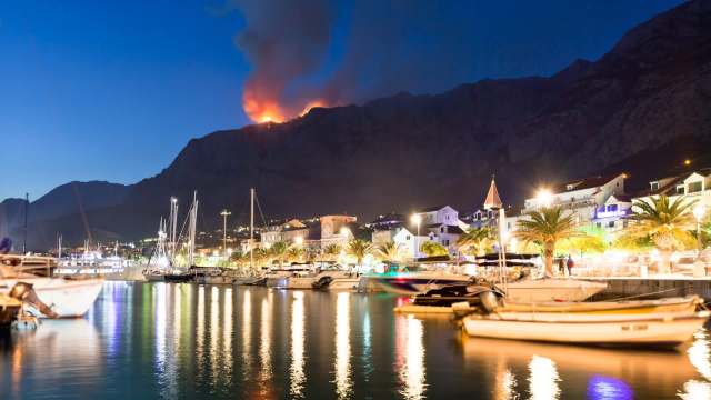 A wildfire on a mountain near boats.