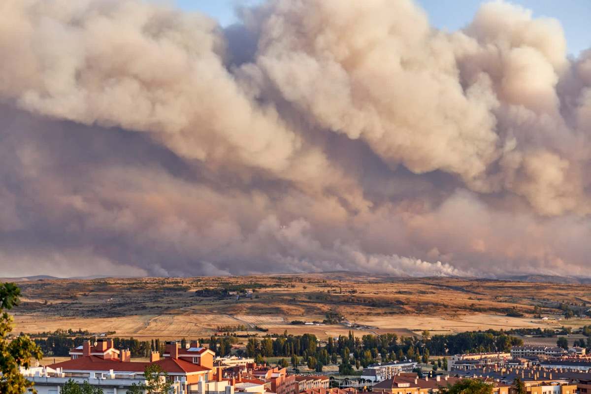 A landscape with smoke-filled skies over a distant fire and residential buildings in the foreground.