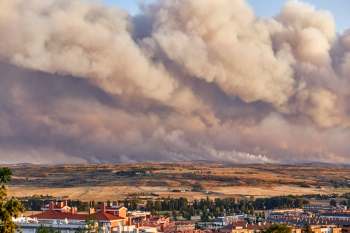 A landscape with smoke-filled skies over a distant fire and residential buildings in the foreground.