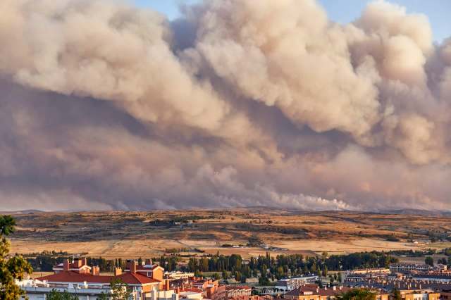 A landscape with smoke-filled skies over a distant fire and residential buildings in the foreground.