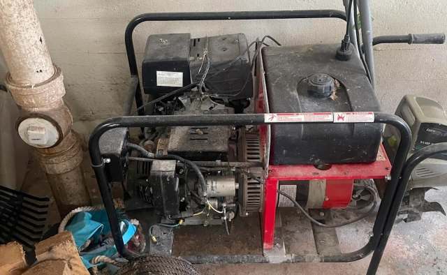 A dusty generator positioned next to a pipe in an indoor setting.