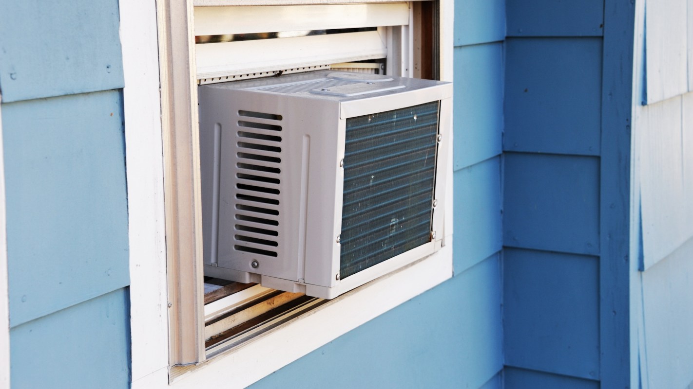 An air conditioning unit is installed in a window of a blue-paneled building.