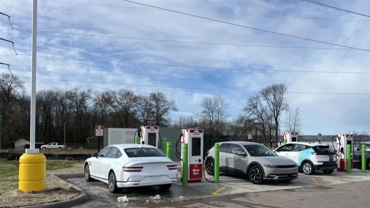 Electric vehicles charging at a station with multiple charging units and a clear sky in the background.