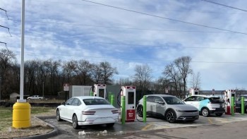Electric vehicles charging at a station with multiple charging units and a clear sky in the background.