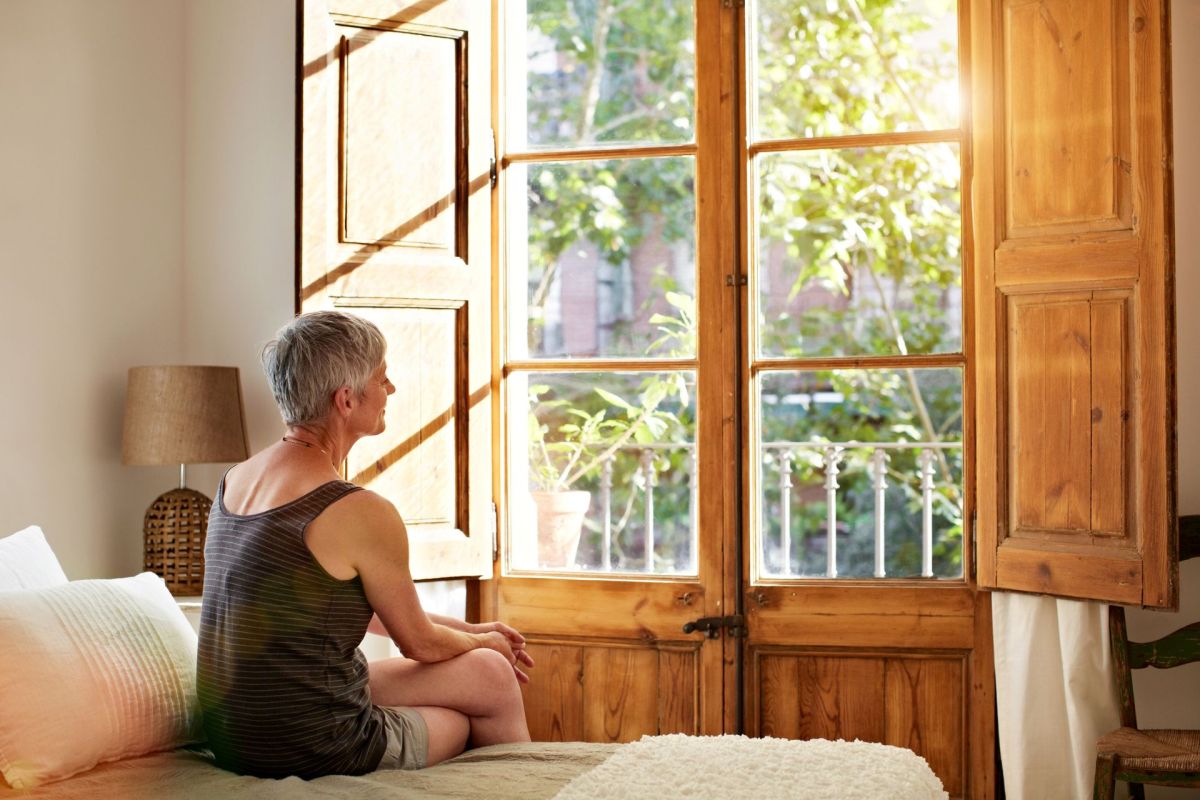 A woman sitting on a bed, looking out a window.