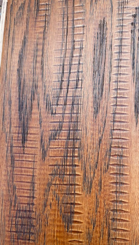 A wooden panel with coarse grain and dents not seen on the sample product. 