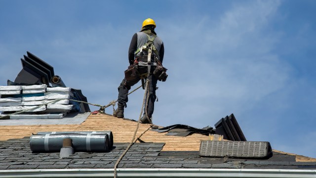 A worker on a sloped roof with safety gear and roofing materials.