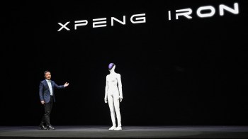 A presenter stands next to a humanoid robot on a stage with the text "XPENG IRON" in the background.