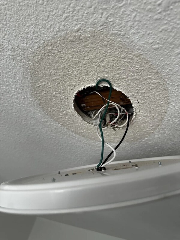 A ceiling hole displaying electrical wires and a surface mount light fixture.