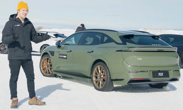 A man stands beside an olive green Zeekr 7GT electric car on snow, with additional cars in the background.