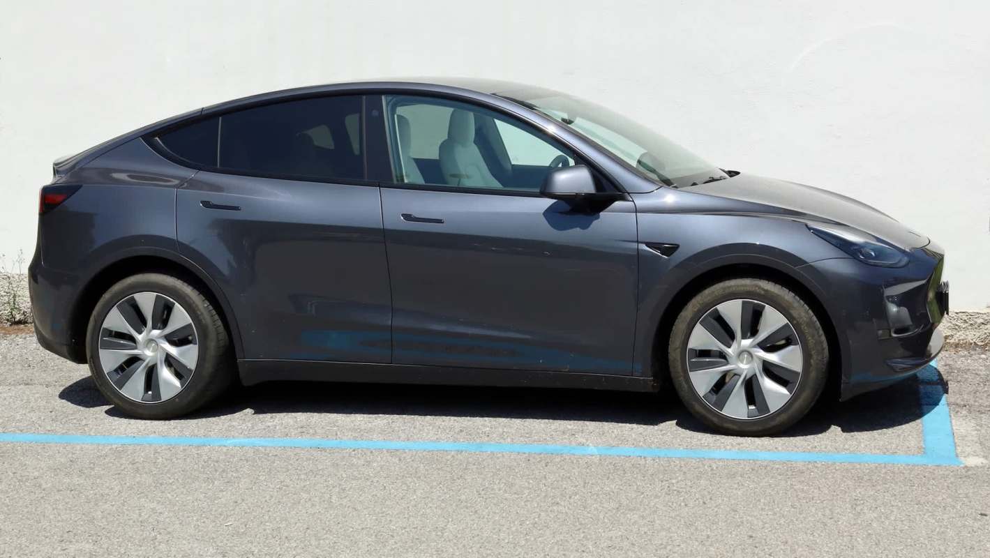 A gray Tesla Model Y parked in front of a white wall.