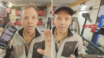 A man holds a smartphone and gestures in a workshop with tools and a bicycle in the background.