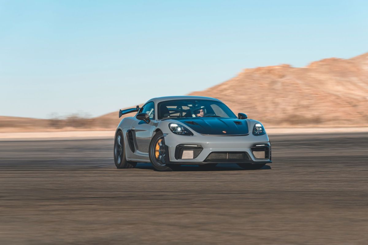 A gray sports car speeds on a track with desert hills in the background.