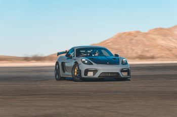 A gray sports car speeds on a track with desert hills in the background.