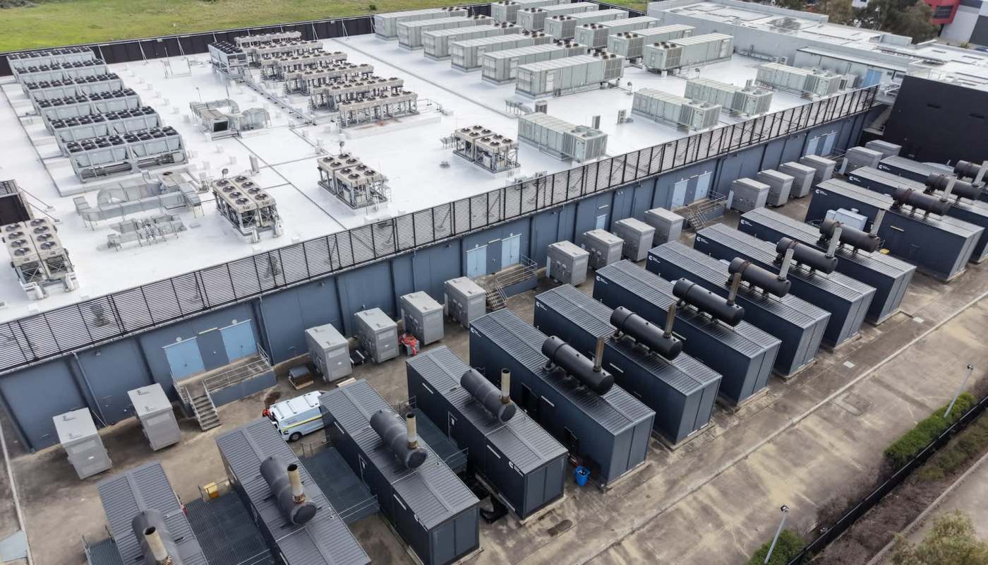 An industrial complex with multiple rooftop cooling units and generator containers arranged in rows.