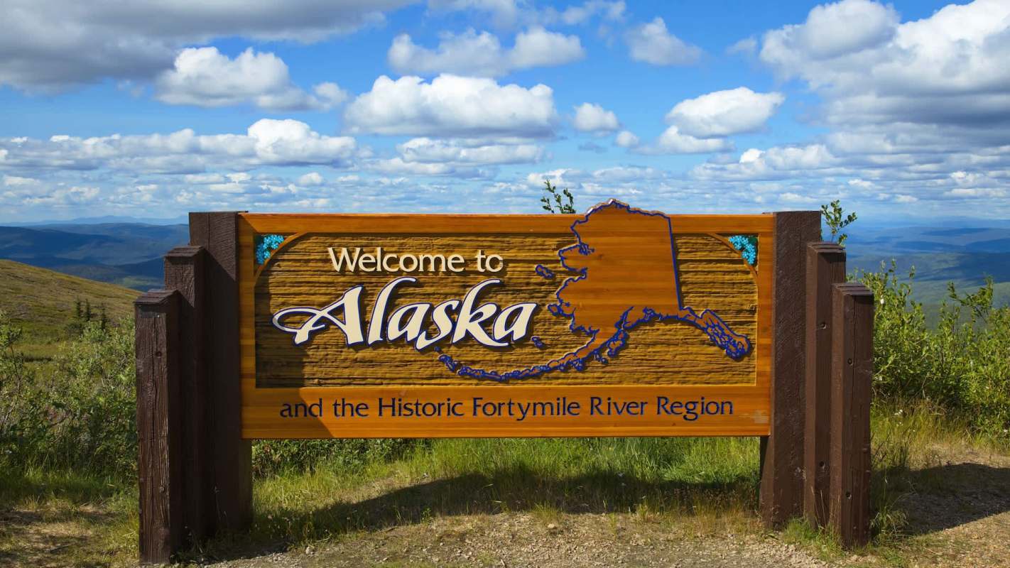 A wooden welcome sign for Alaska with the text and a map outline of the state.