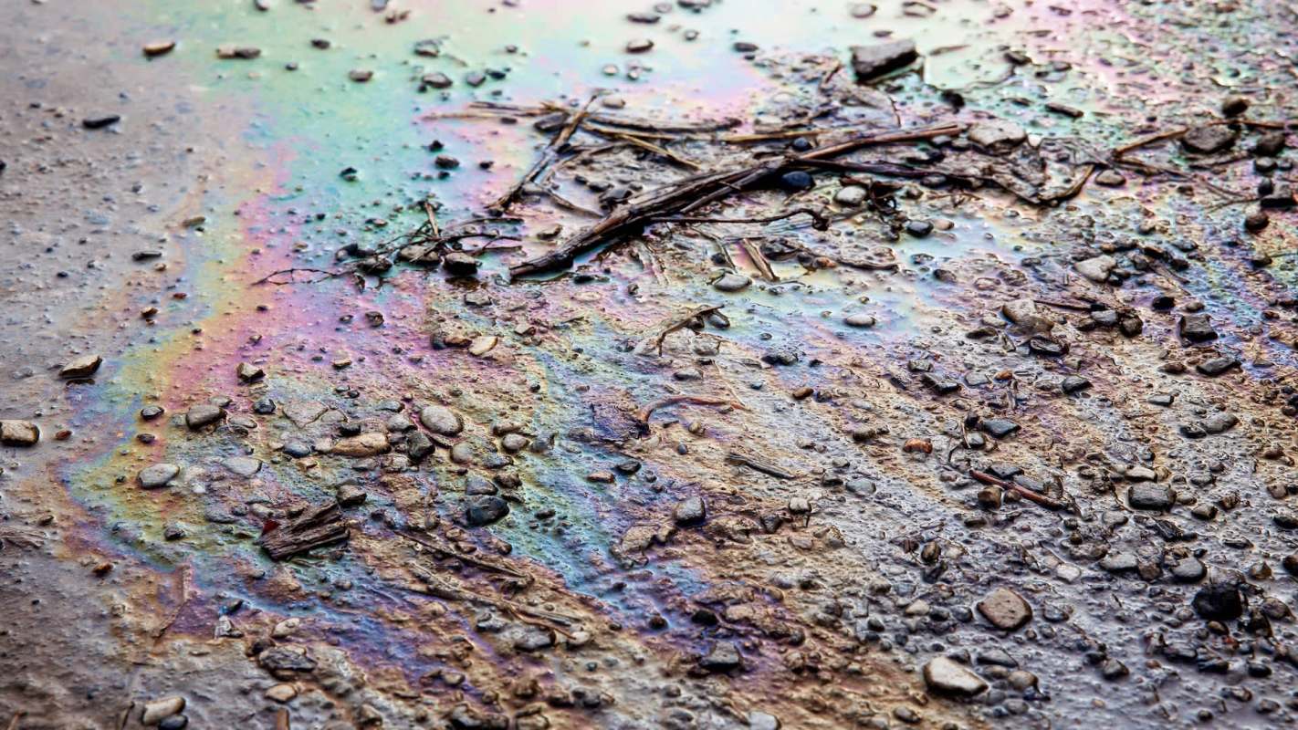 An oily rainbow sheen on wet ground mixed with small stones and debris.