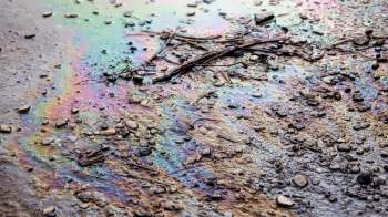 An oily rainbow sheen on wet ground mixed with small stones and debris.