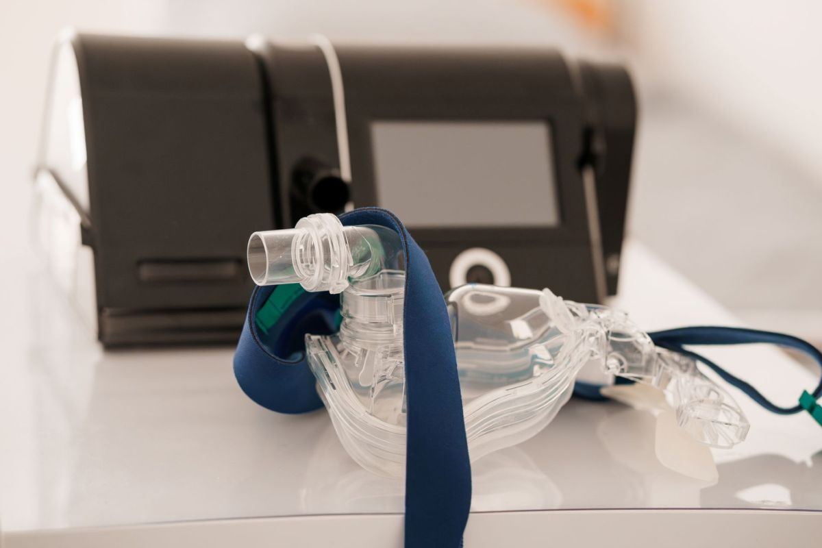 A clear sleep apnea mask with a blue strap placed beside a black CPAP machine.
