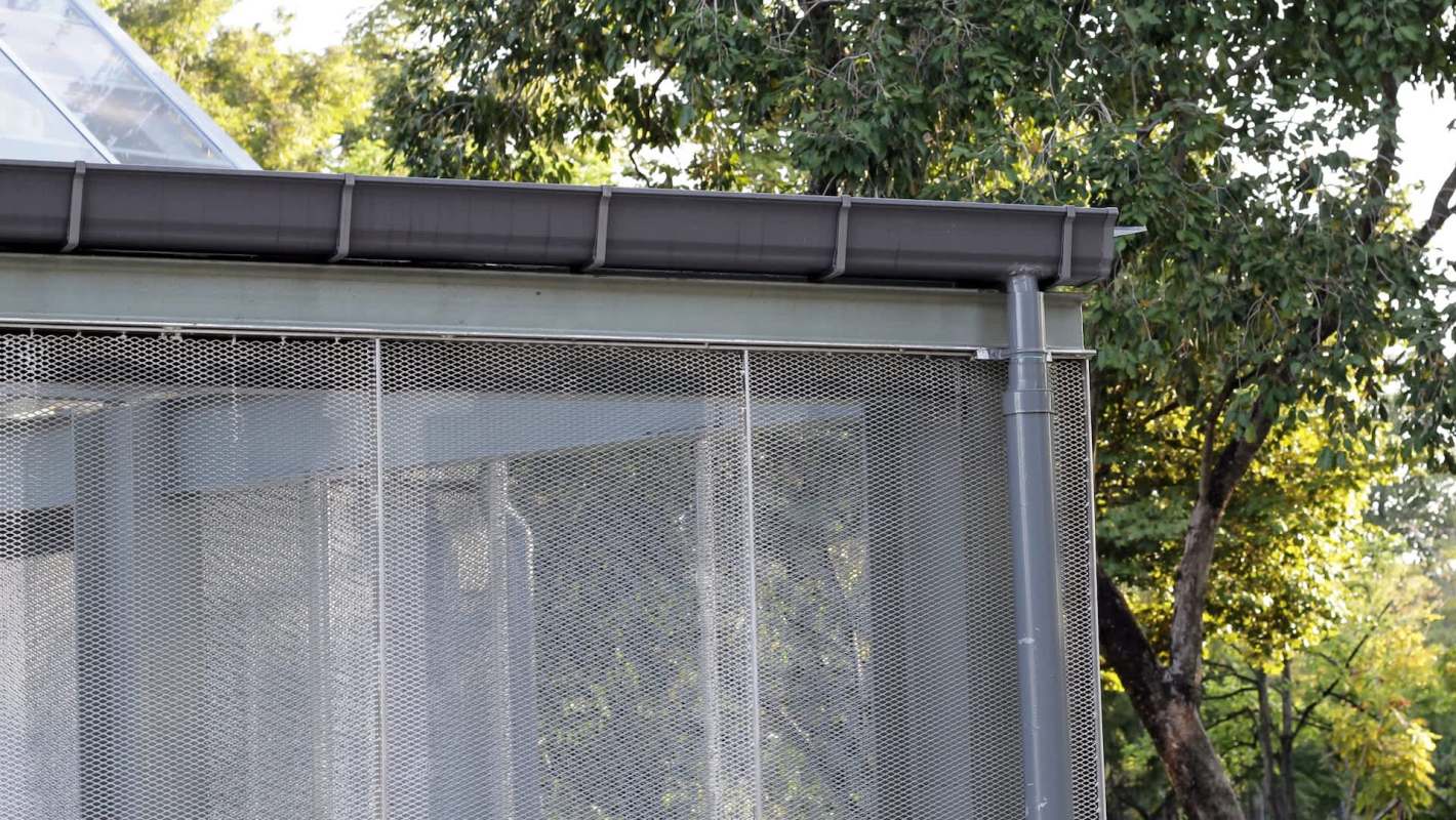 A metal mesh enclosure around a house with a drainage pipe, surrounded by trees.
