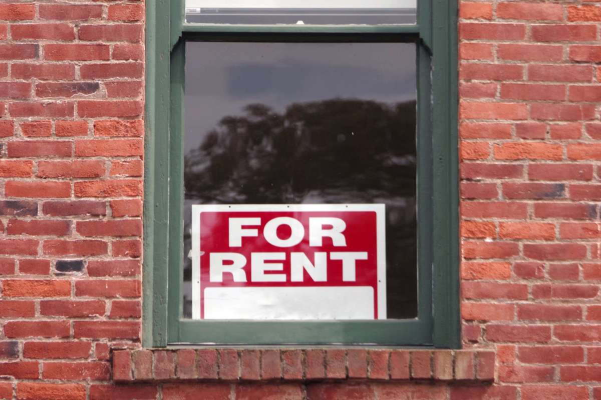 A "For Rent" sign in the window of a brick building.