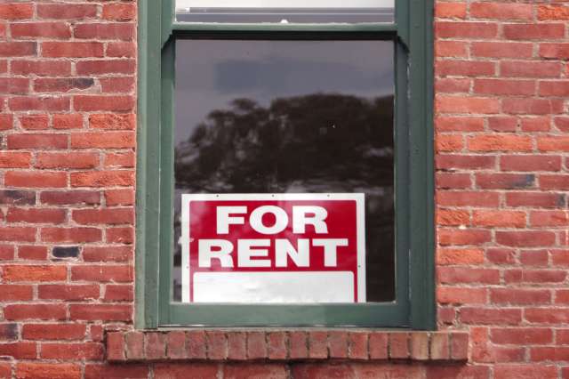 A "For Rent" sign in the window of a brick building.