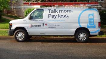 A Comcast service van parked on the street, featuring a ladder on the roof and promotional text on the side.